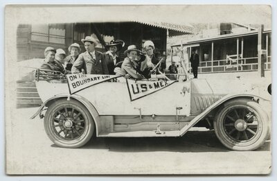 Automobile passengers with "On the boundary line" and "U.S. & Mex." pennants